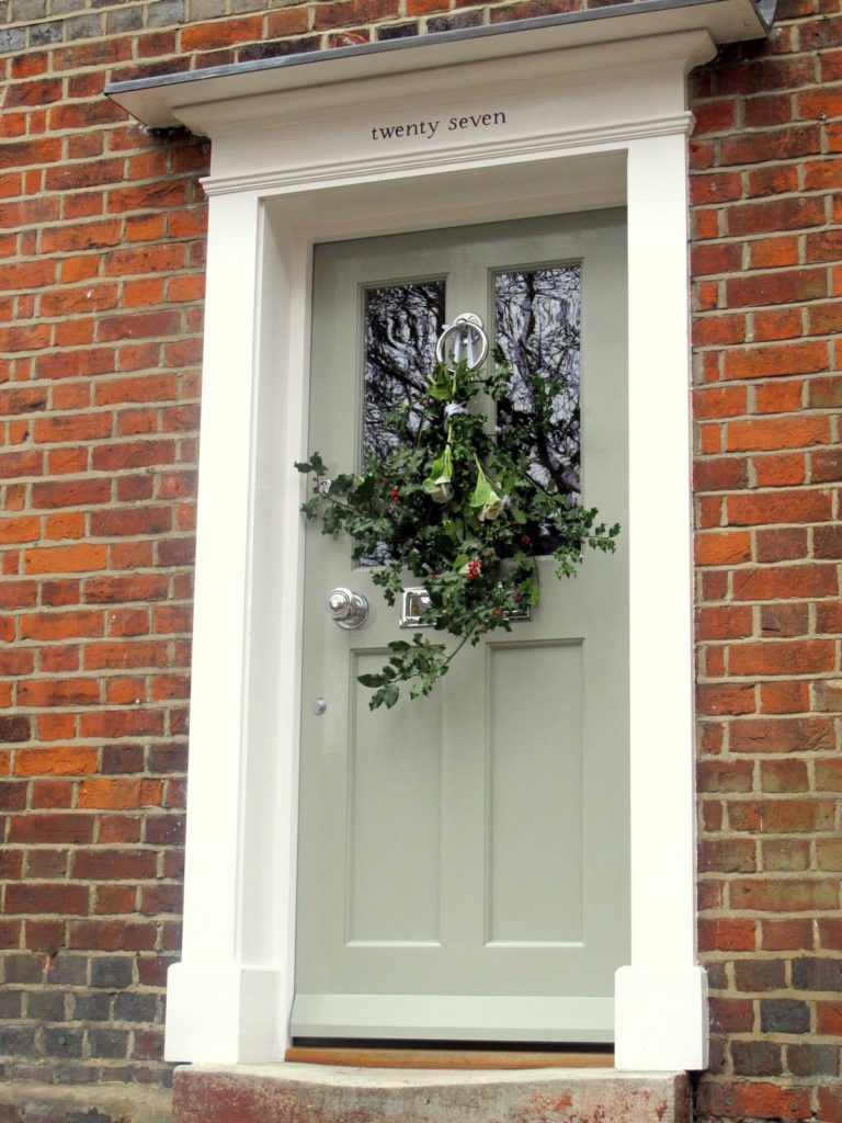 brick home with sage green front door with wreath