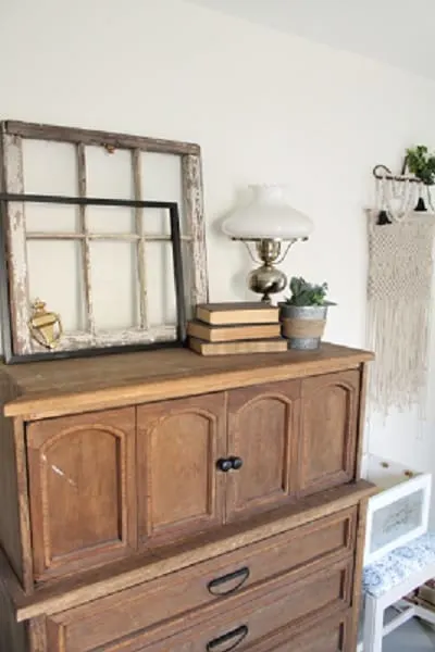 A room with Alabaster painted walls and a wood dresser with lamp and books on top.