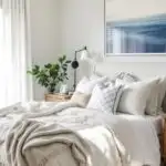 neutral bedroom with a cozy bed , nightstand with a plant and navy blue art over the bed