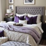 A feminine neutral bedroom that has a bed , art, night stands and a gray and purple color palette