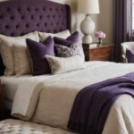 A feminine neutral bedroom that has a bed , ottoman and with purple and wood accents