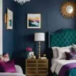 bedroom with dark blue walls, gold chandelier, and bed in a jewel toned color palette