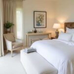 A neutral bedroom with a bed and large window that is decorated like a hotel room